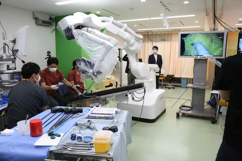 【MIL名古屋のトレーニング施設】中央の白い機械が手技をおこなうロボットアーム。黒い手術台には胃がんの臓器モデルが置かれ、術部の拡大画像が右側のモニターに映し出されている（写真提供：宇山医師）