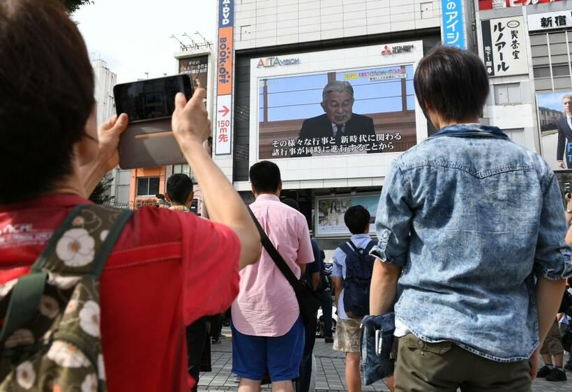 2016年8月8日、新宿街頭の大画面で流れる天皇陛下（当時）のビデオメッセージを見上げる人々　（ｃ）朝日新聞社